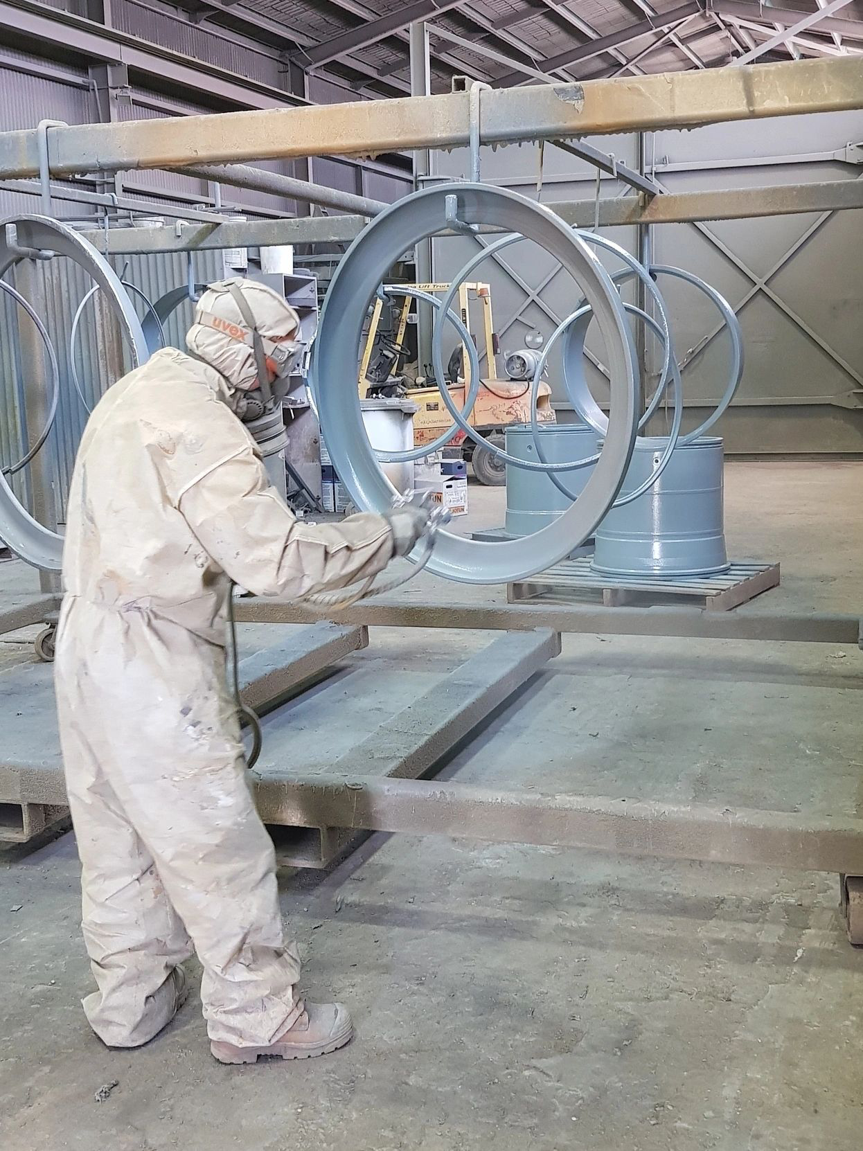 A man wearing a gas mask is spray painting a piece of metal