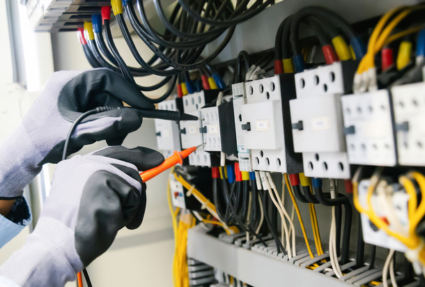 Gloved technician testing electrical panels with orange probe in a wiring cabinet