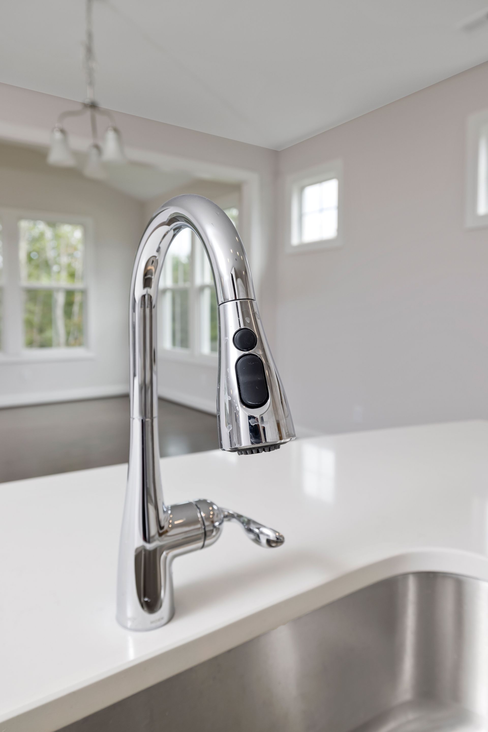 Chrome kitchen faucet with pull-down spray over a white countertop and stainless sink