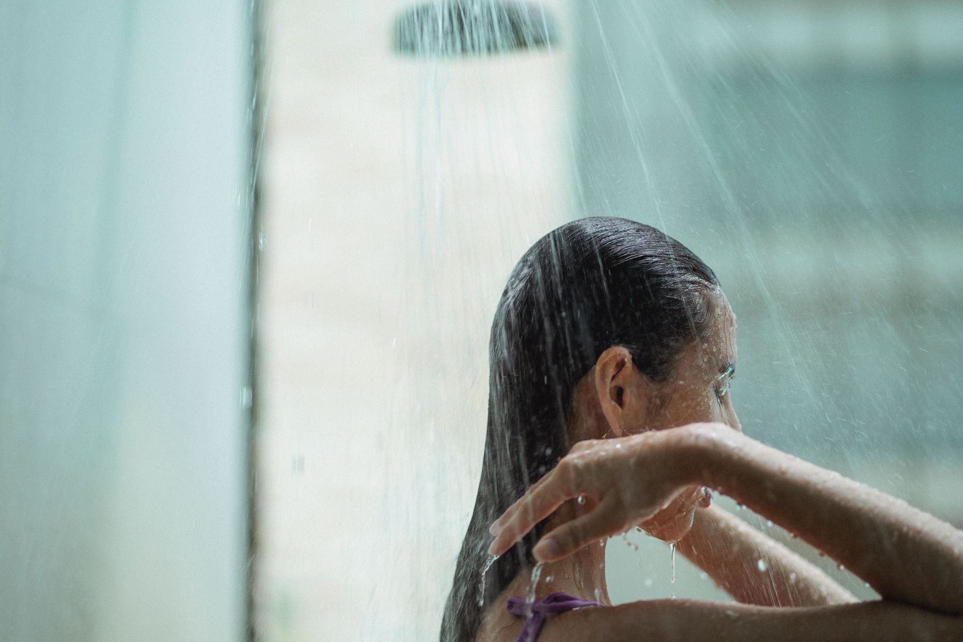 Person washing hair under a shower, with water running over their head and shoulder.