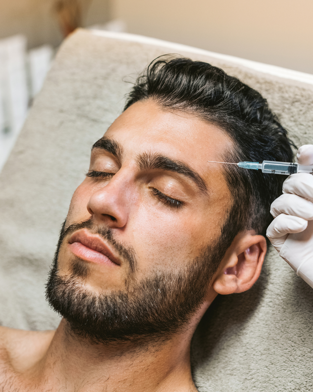 Man receiving a facial injection near the temple while lying on a treatment table