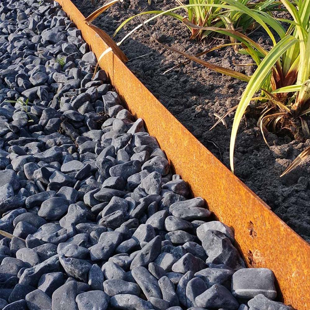 A rusty metal landscape edging strip separating dark gray gravel from a garden bed with green plants.