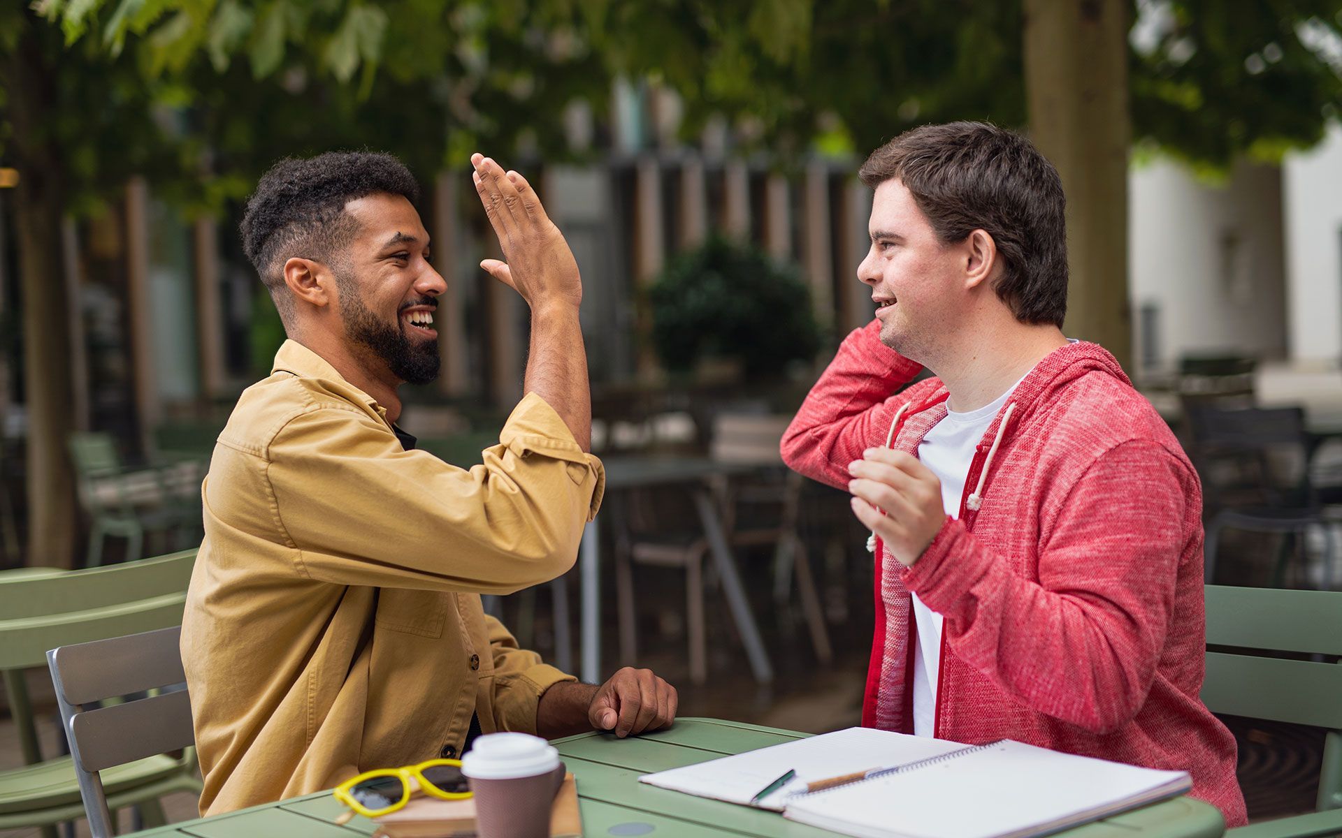 Two men are sitting at a table giving each other a high five.