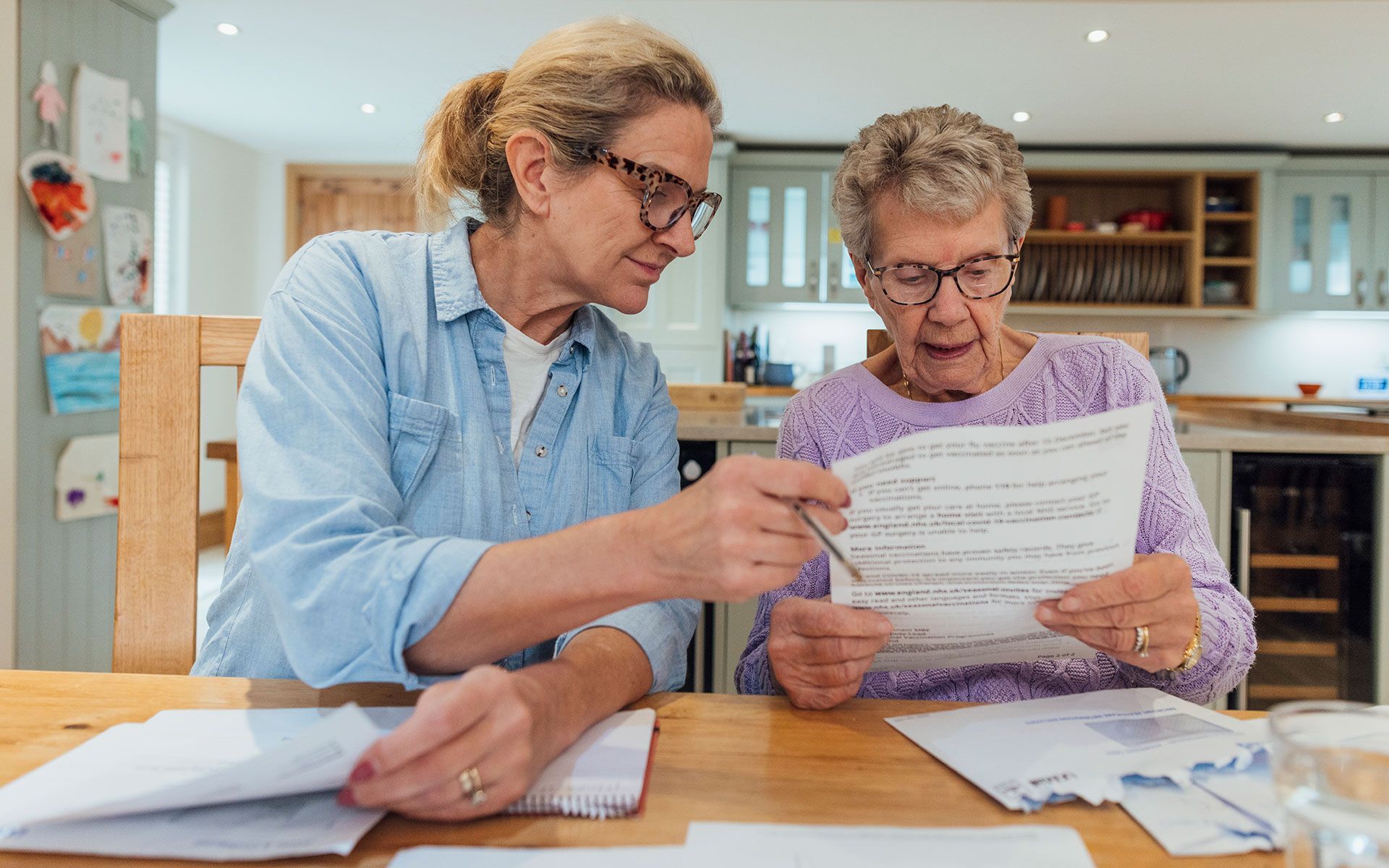 Two older women are sitting at a table looking at a piece of paper.