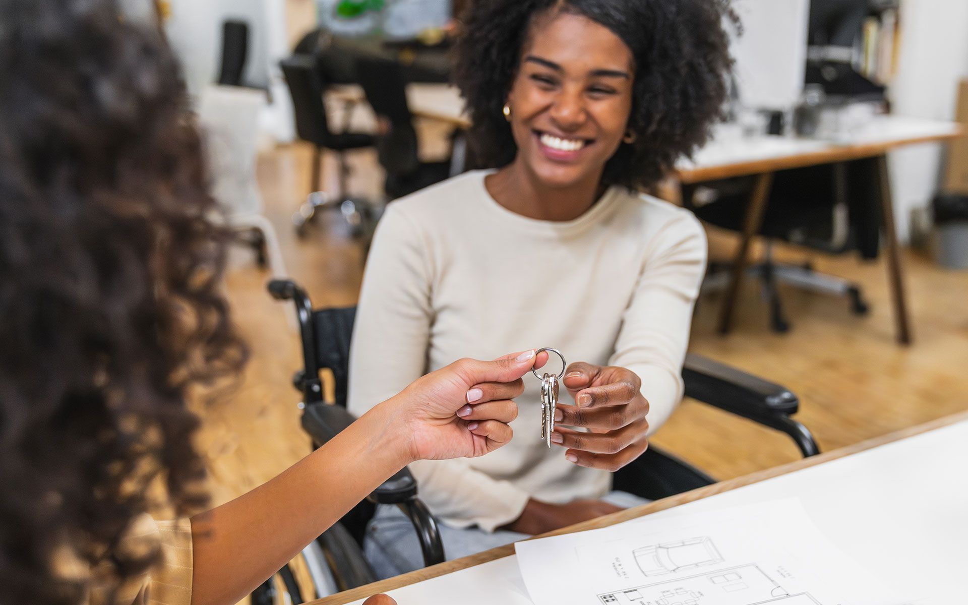 A woman in a wheelchair is sitting at a table holding a bunch of keys.