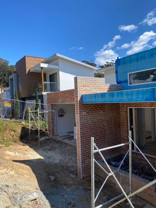 Partially built modern house with brick walls, blue roofing, and a metal gate on a hillside