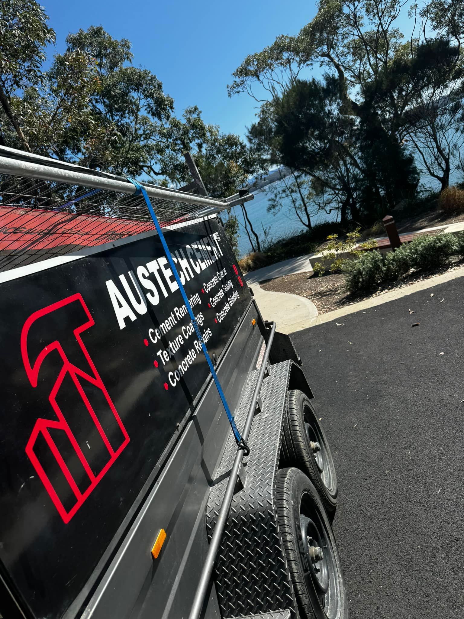 Black off-road vehicle with the Austech cement logo parked on a sunny roadside near trees and water on the south coast
