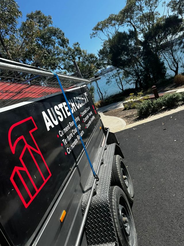 Black trailer with Austech Cement logo parked by a road on the South Coast, with trees and blue sky in the background