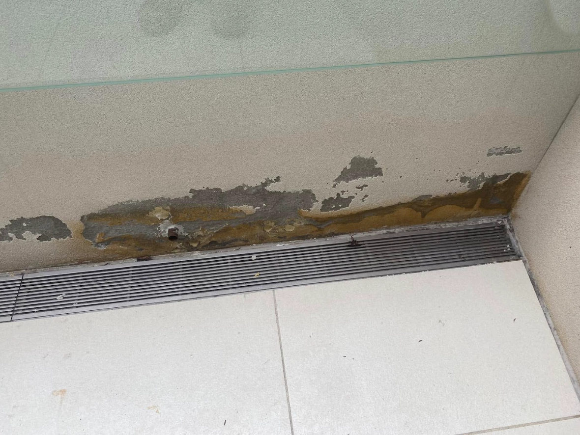 Damaged wall with peeling paint and mould above a floor vent and white tiles