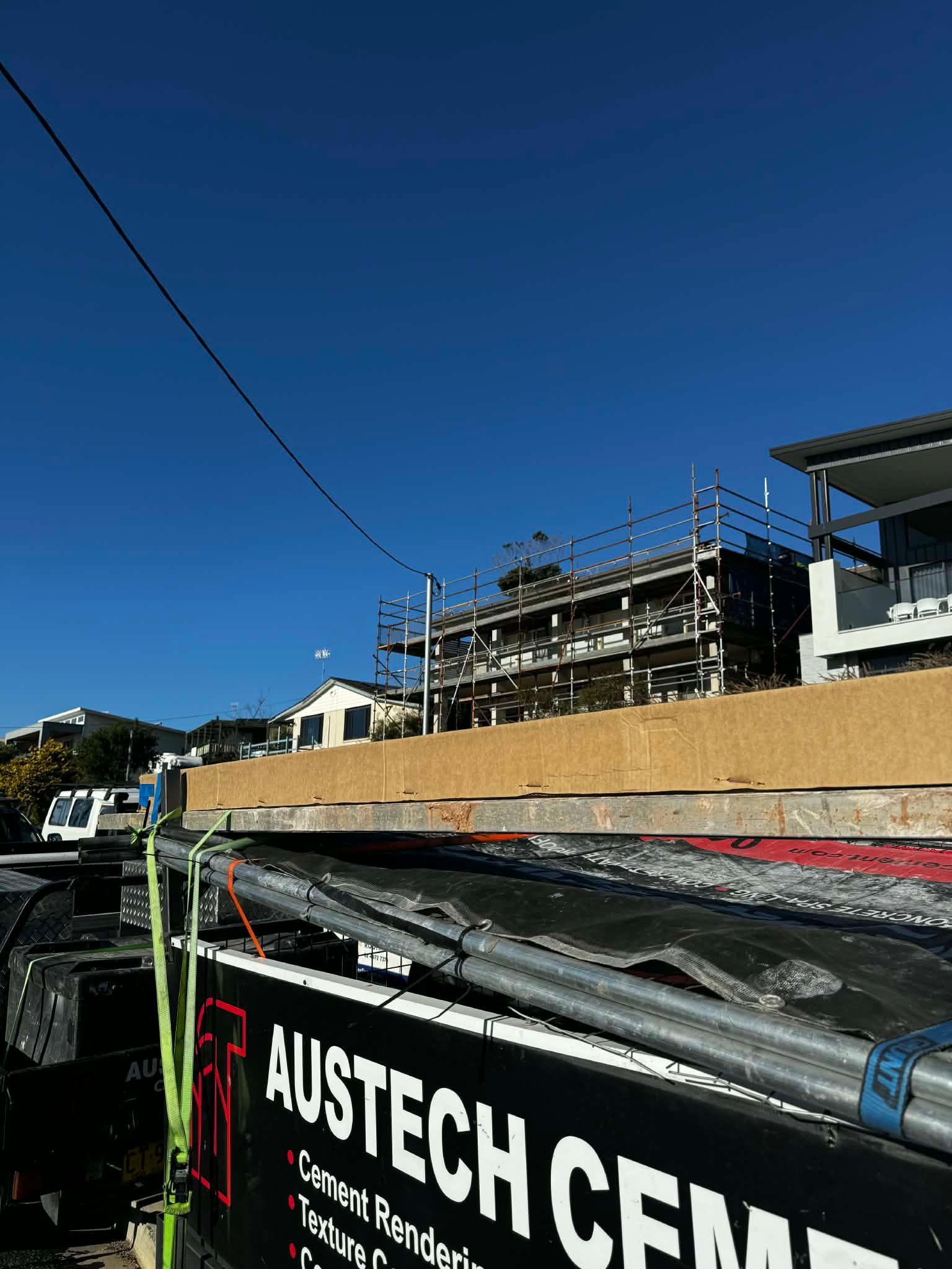 Street-level construction site under a clear blue sky, with a partially built structure and AUSTECH banner in foreground