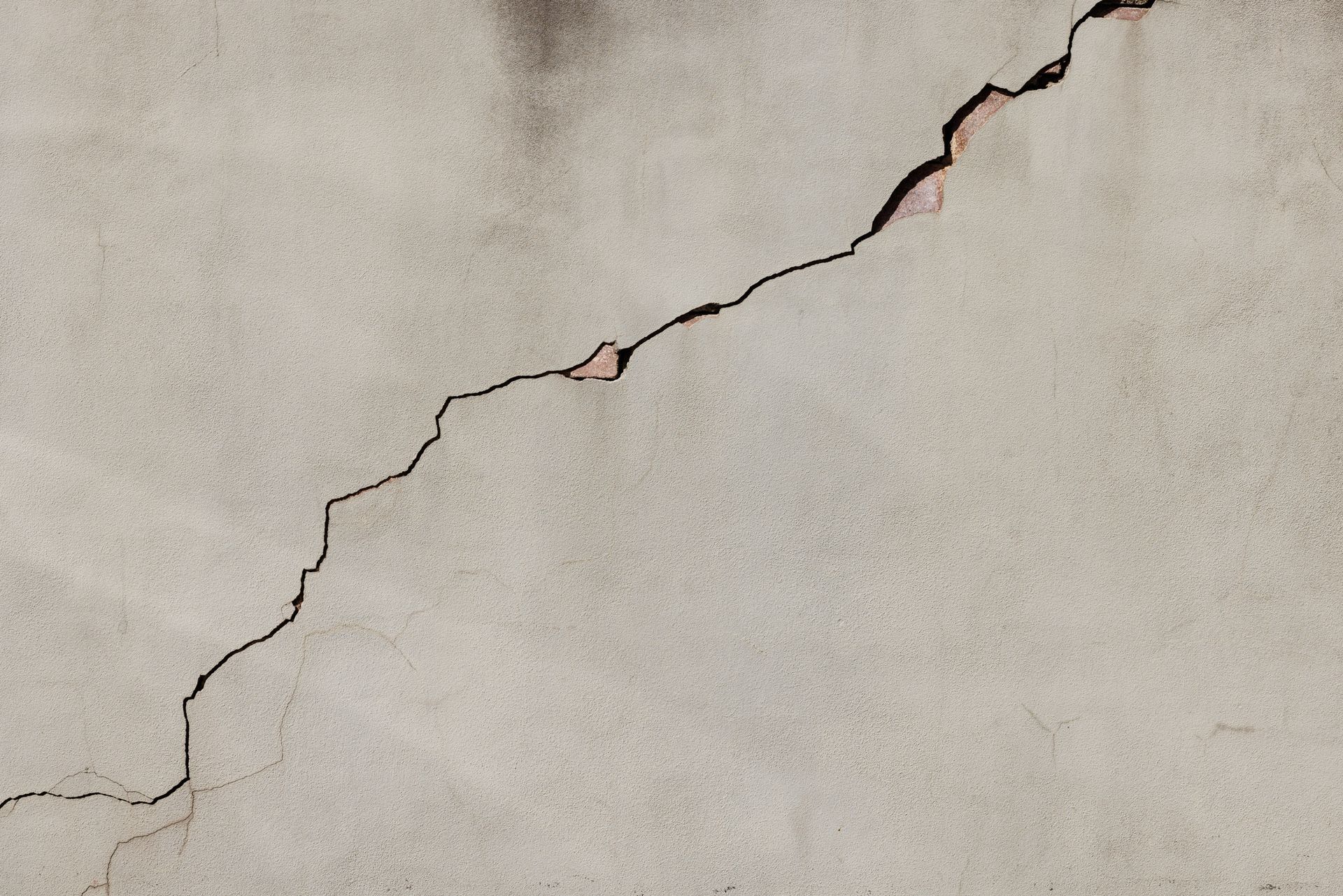 Cracked beige plaster wall with a diagonal fissure and exposed reddish edges