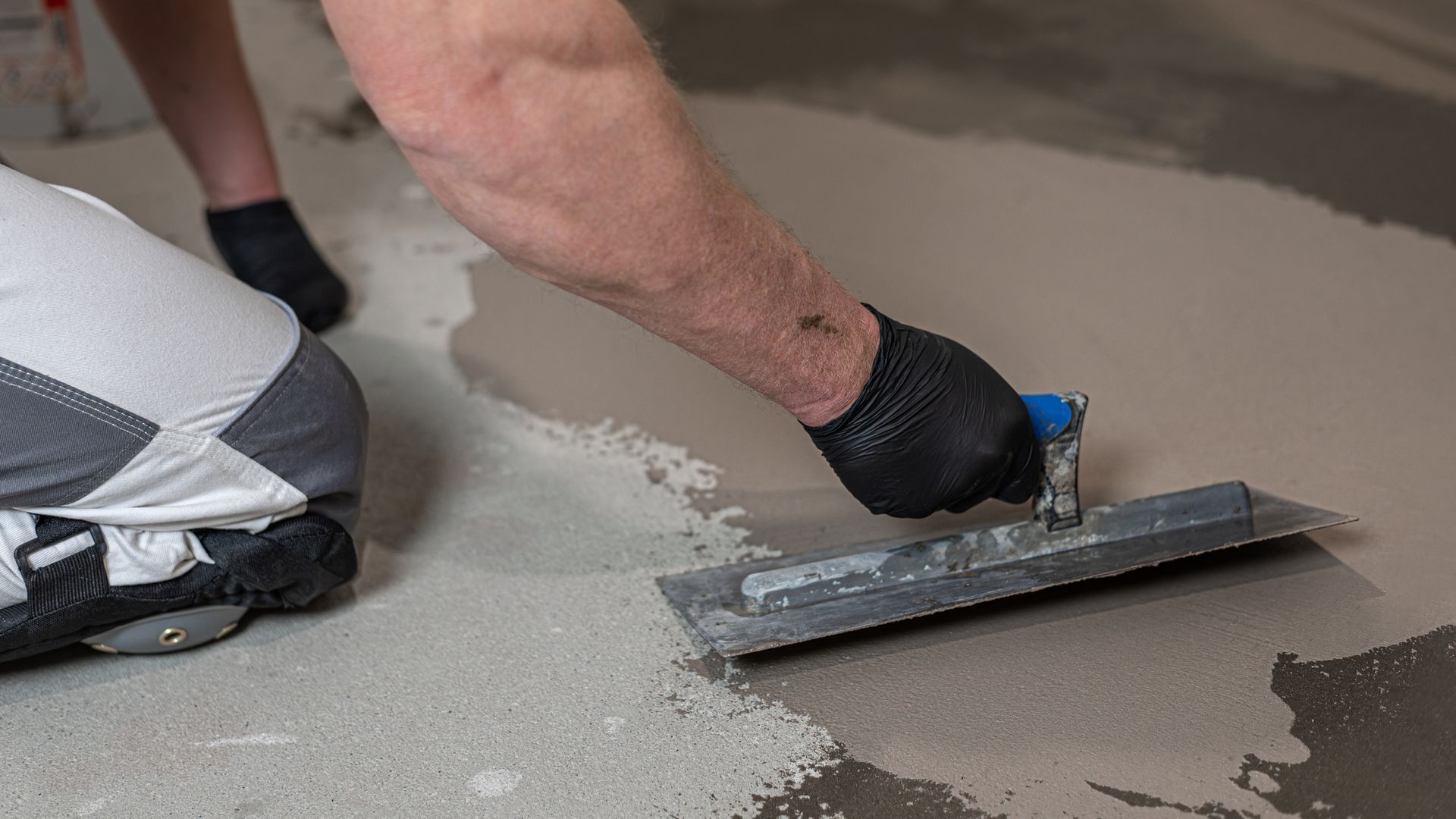 Worker smoothing wet concrete with a trowel on a floor surface.
