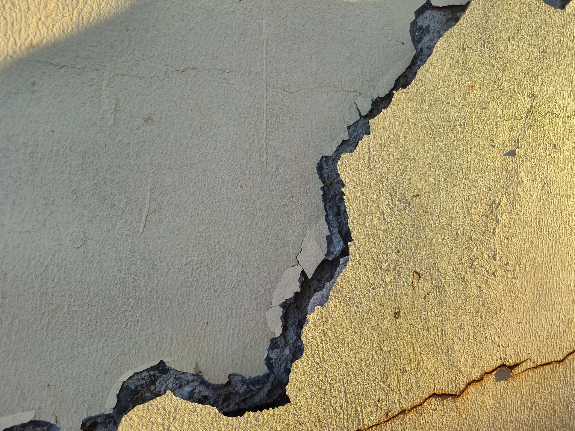 Cracked concrete wall with peeling gray and yellow paint, showing a jagged split between surfaces