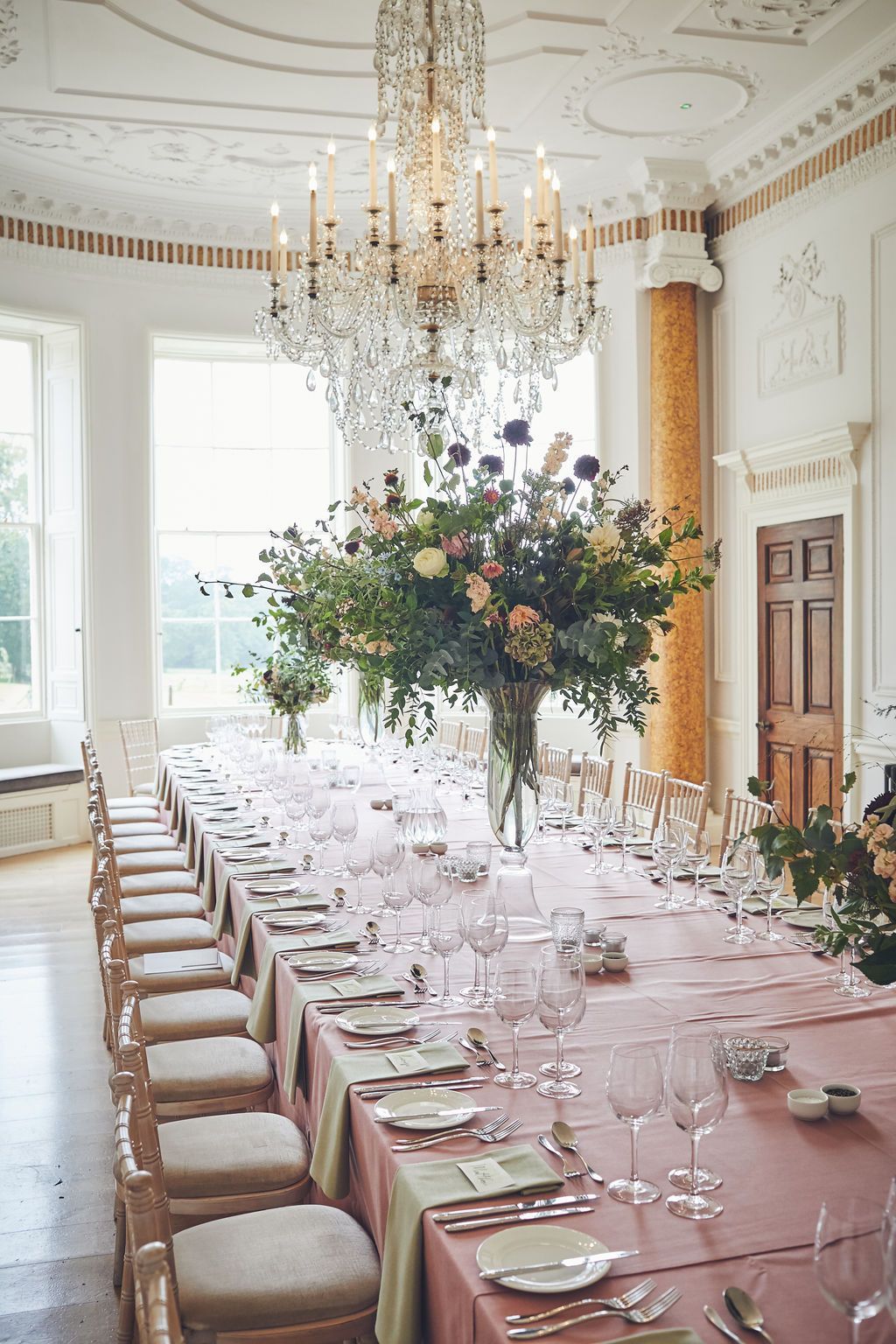 a long table with a vase of flowers on top of it in a room with a chandelier .