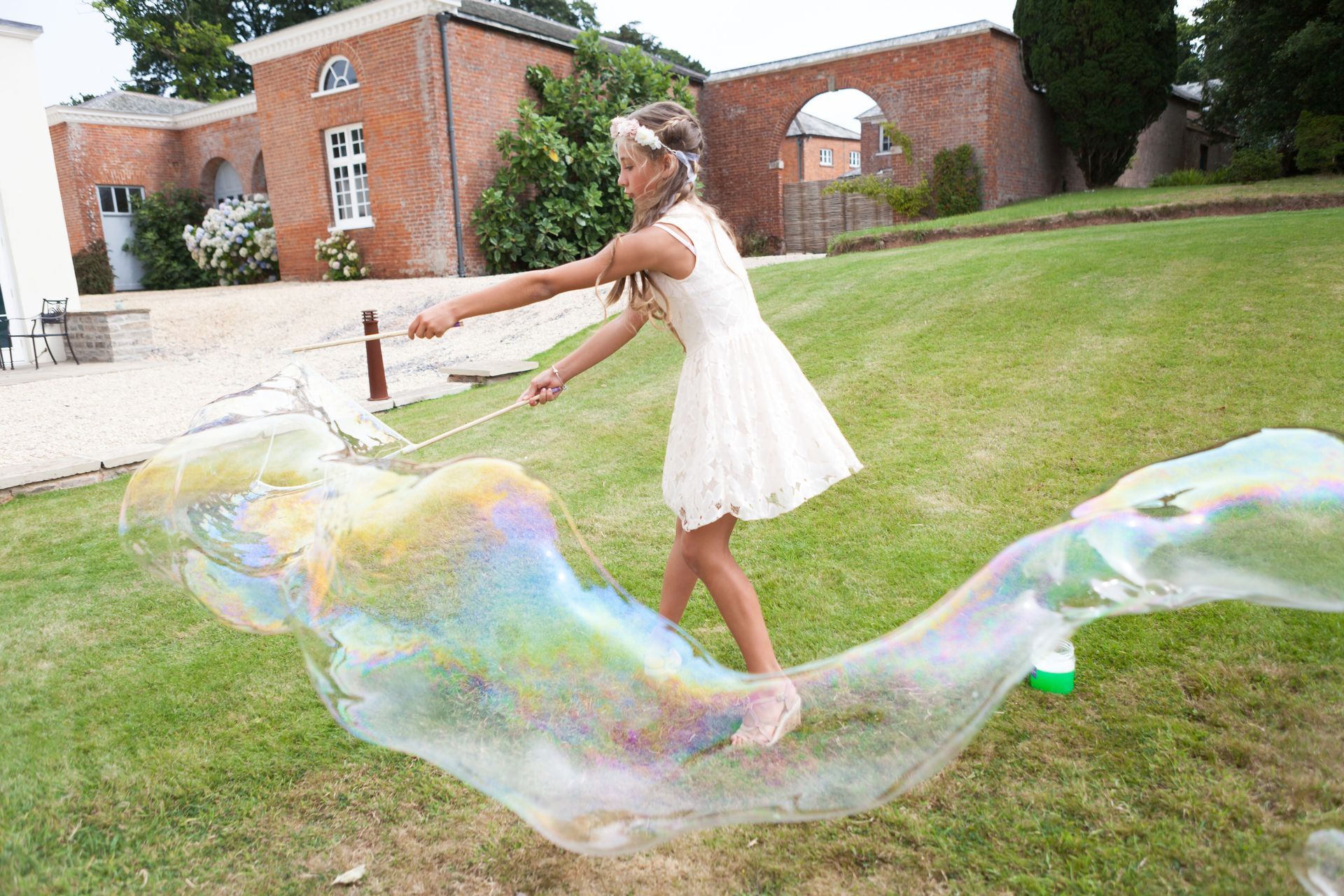 a little girl in a white dress is blowing soap bubbles in the grass .