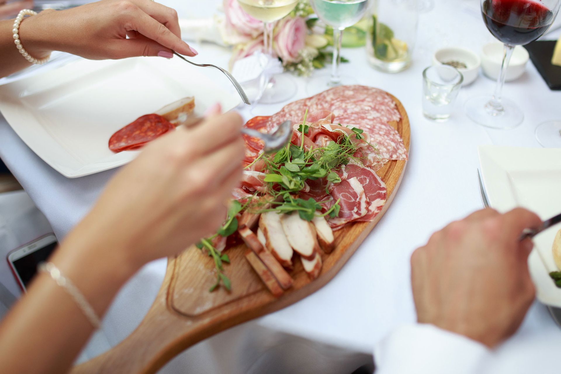 a man and a woman are sitting at a table eating food from a wooden cutting board .