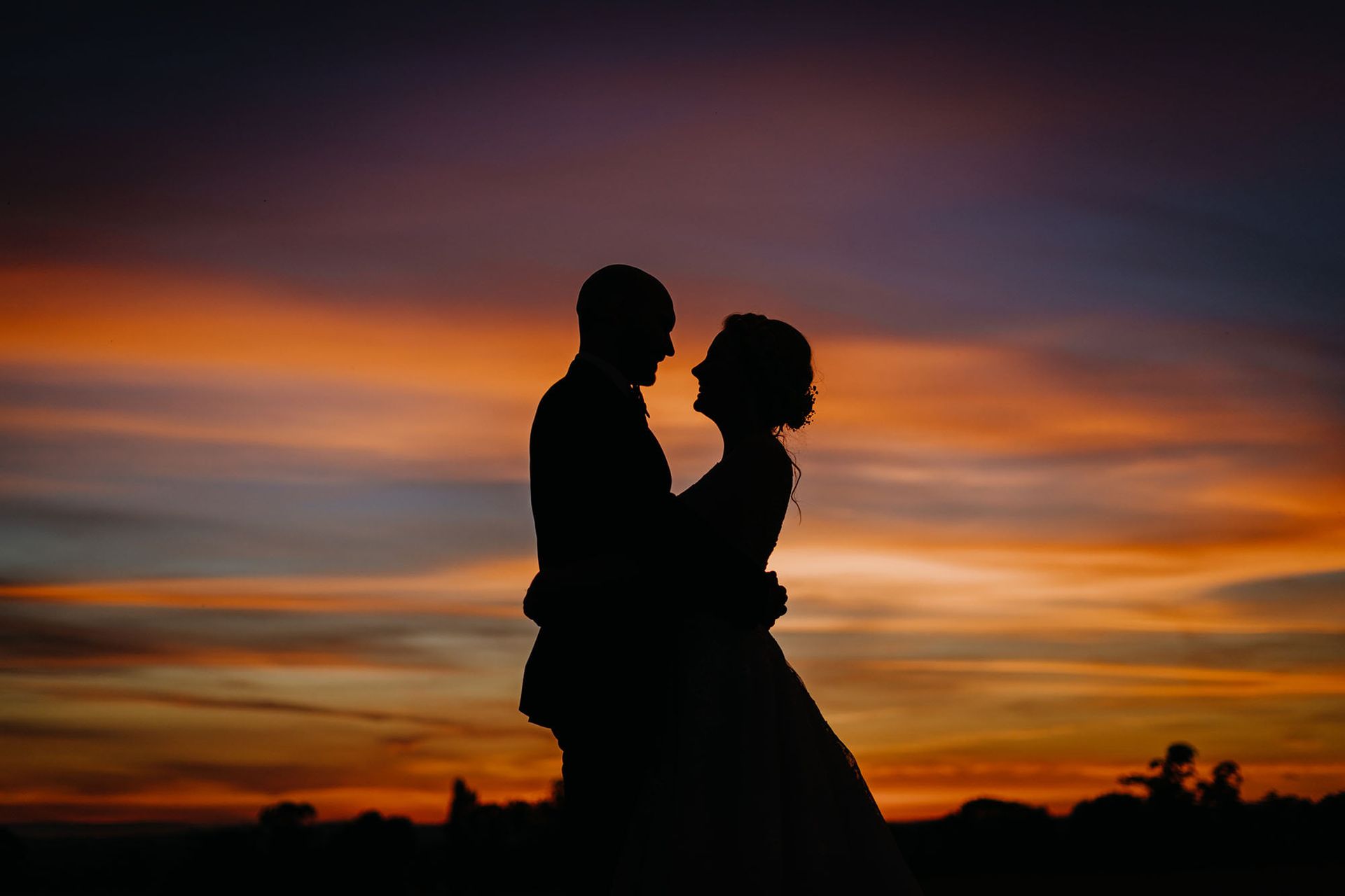 a bride and groom are hugging each other at sunset .