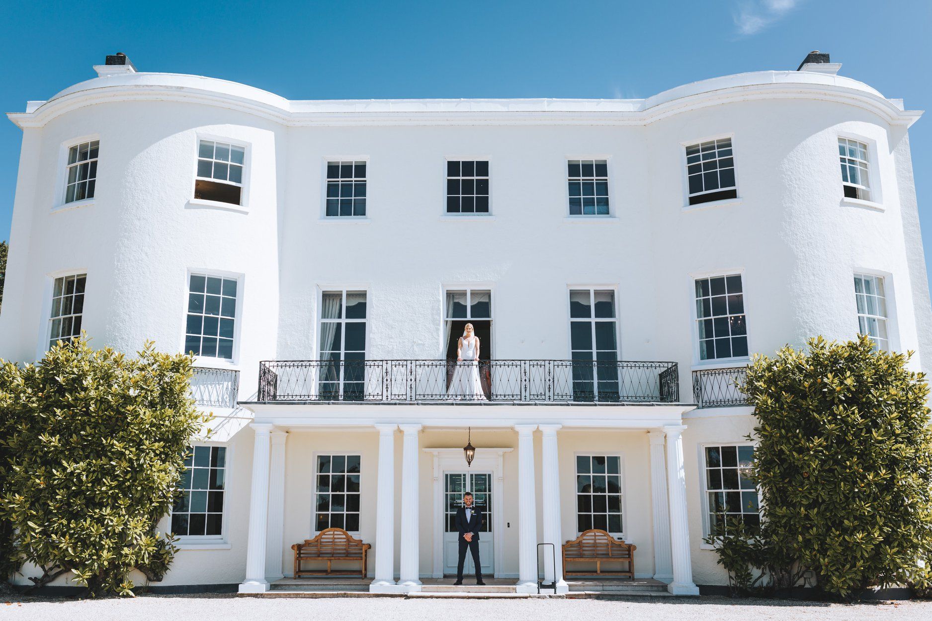 a bride and groom are standing in front of a large white house .