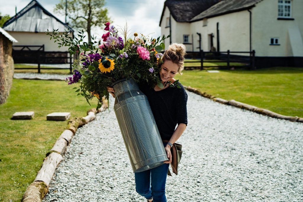 a woman is carrying a large bucket of flowers down a gravel road .