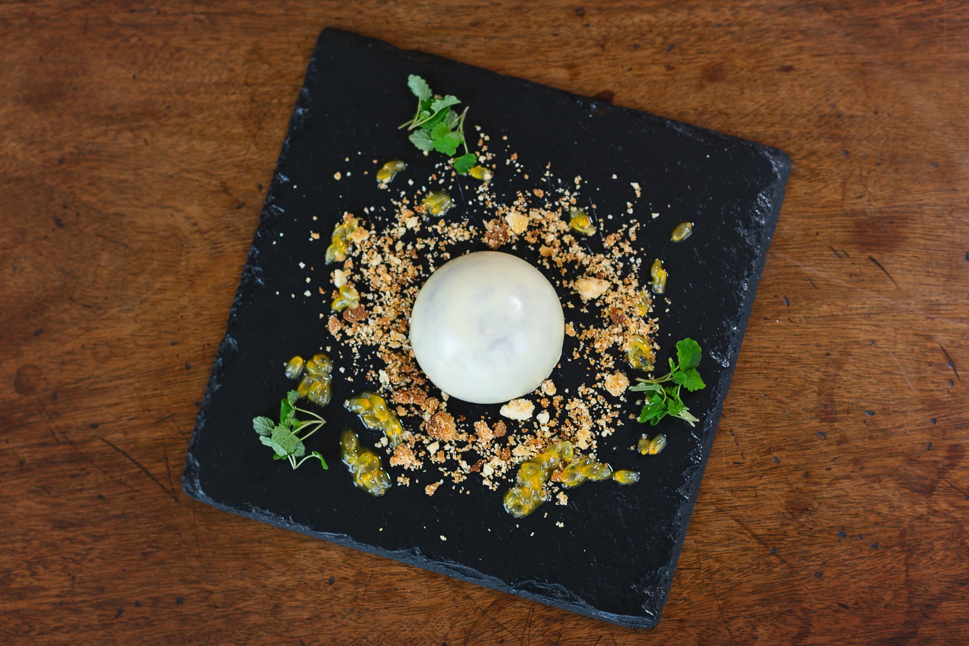 a black plate topped with a white ball and nuts on a wooden table .