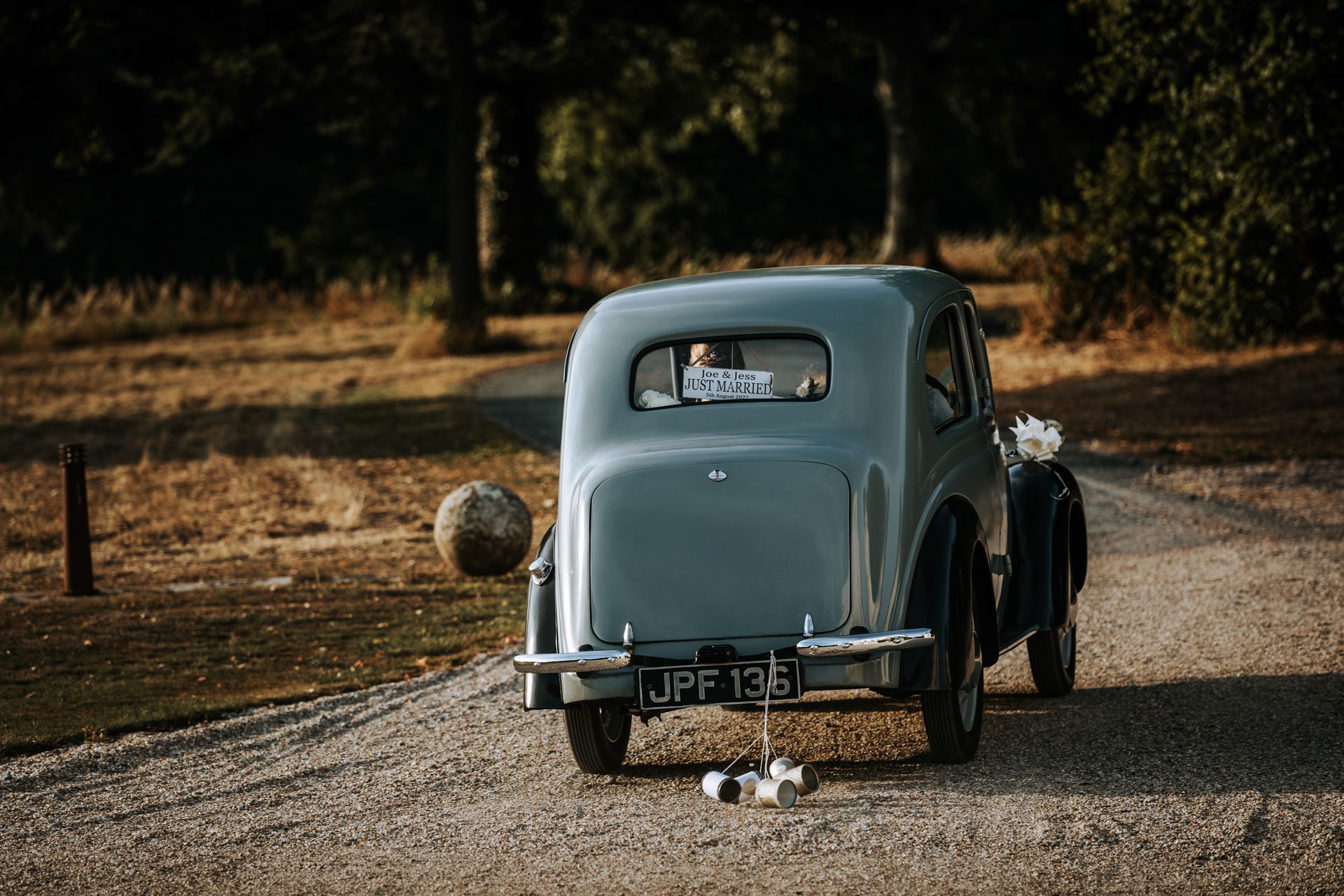 a bride and groom are driving down a gravel road in an old car .