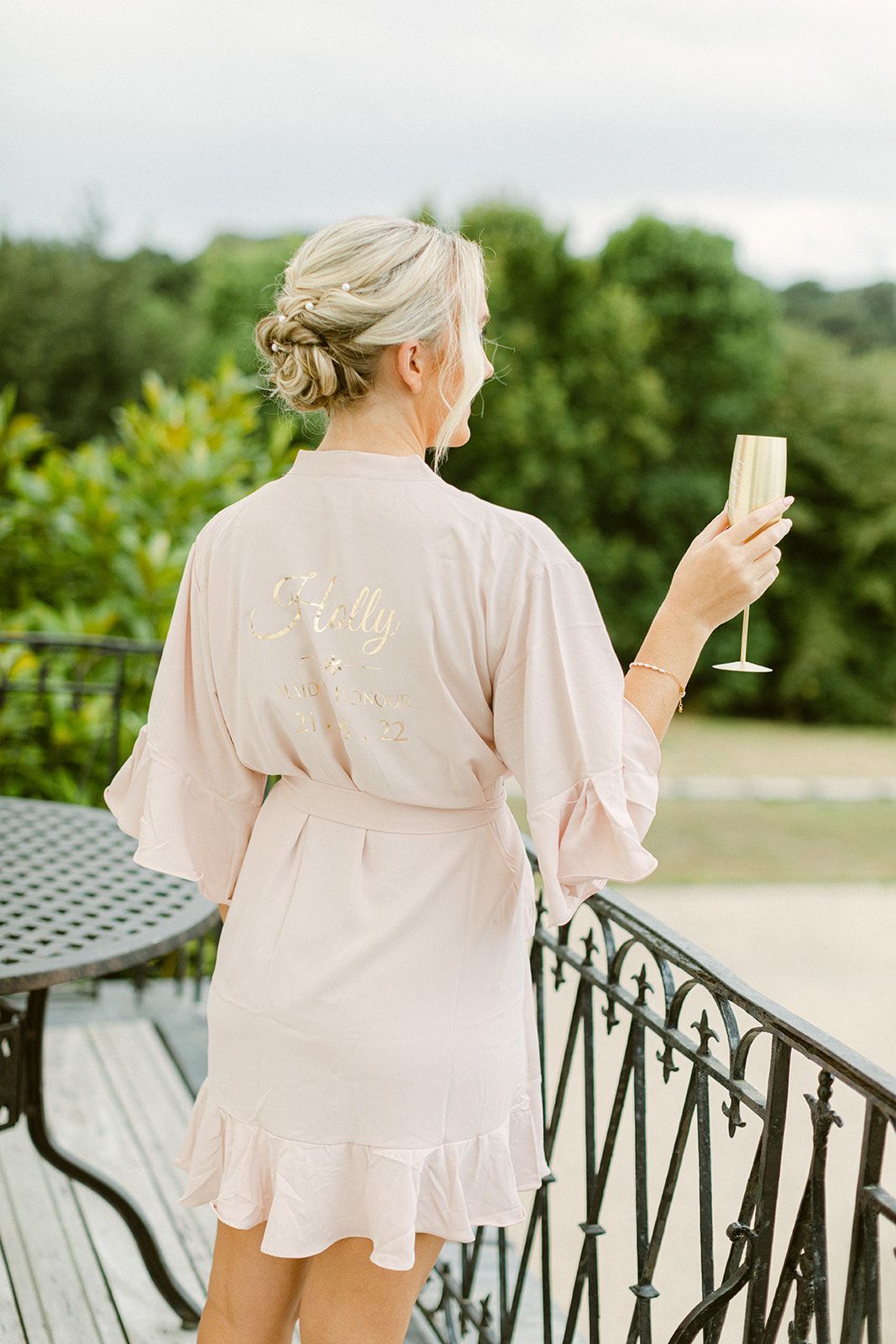 a woman in a pink robe is standing on a balcony holding a glass of champagne .