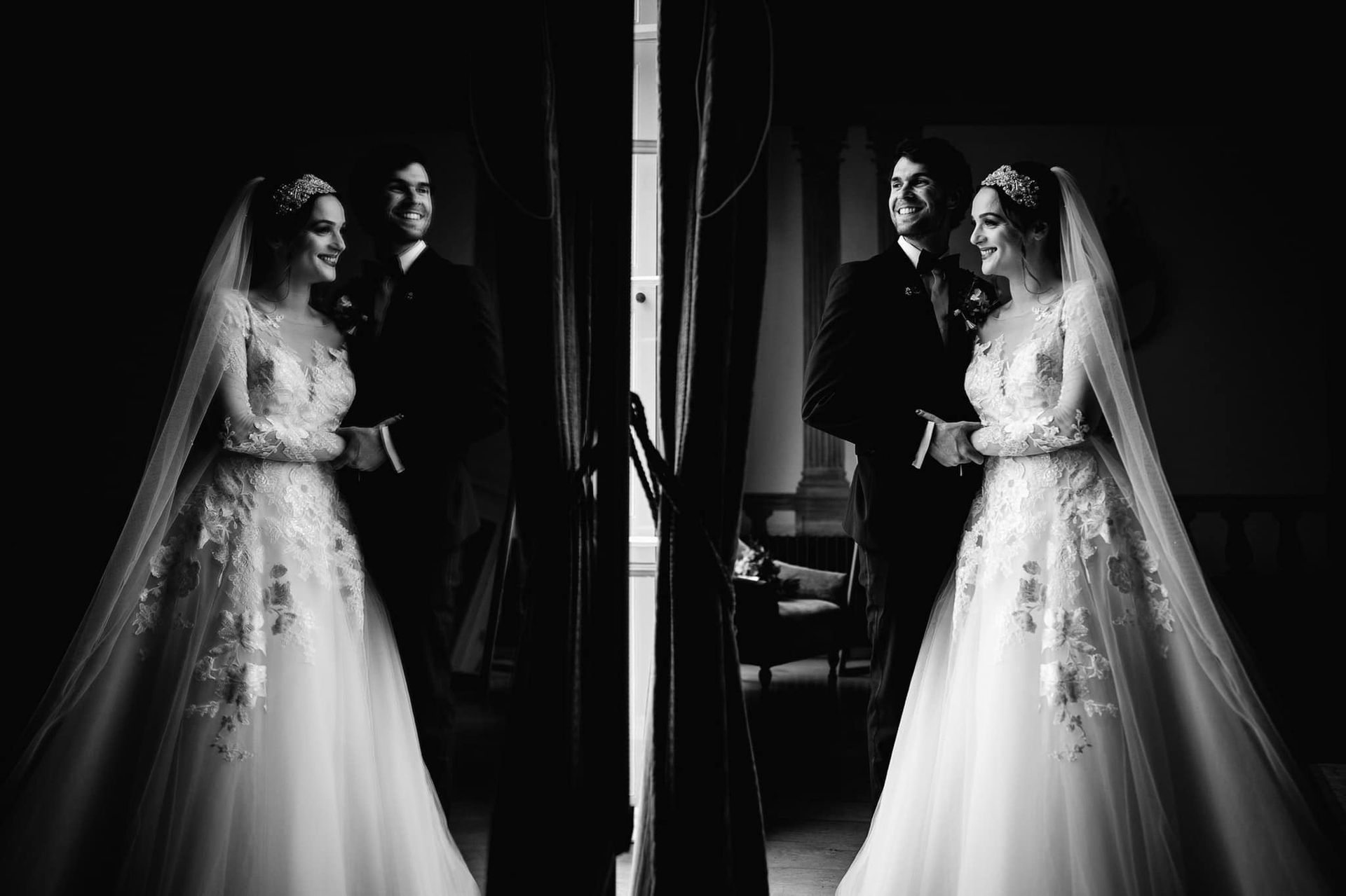 a black and white photo of a bride and groom standing in front of a window .