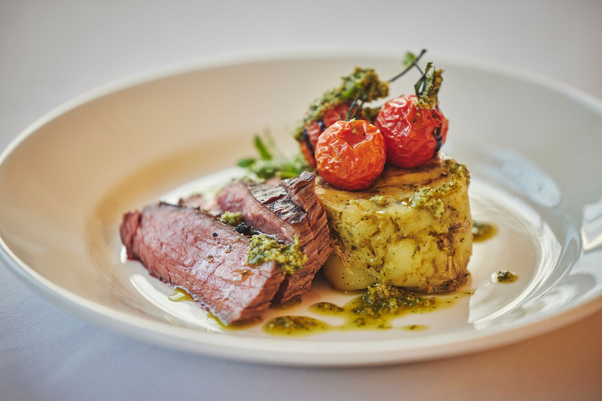 a white plate topped with meat , potatoes and tomatoes .