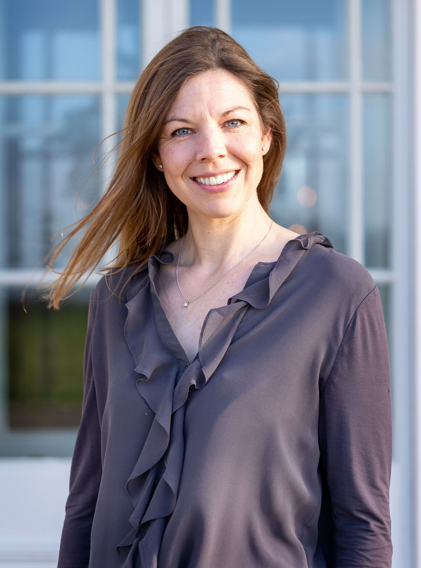 a woman in a ruffled shirt is smiling in front of a window .