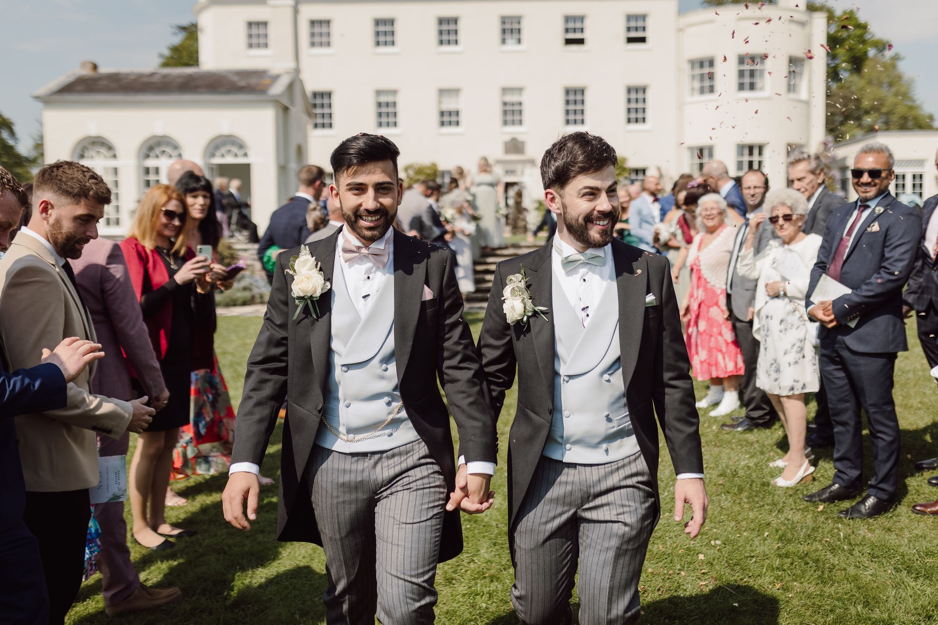 two men in tuxedos are holding hands while walking down the aisle at a wedding .