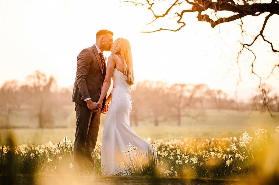 a bride and groom are kissing in a field of flowers at sunset .