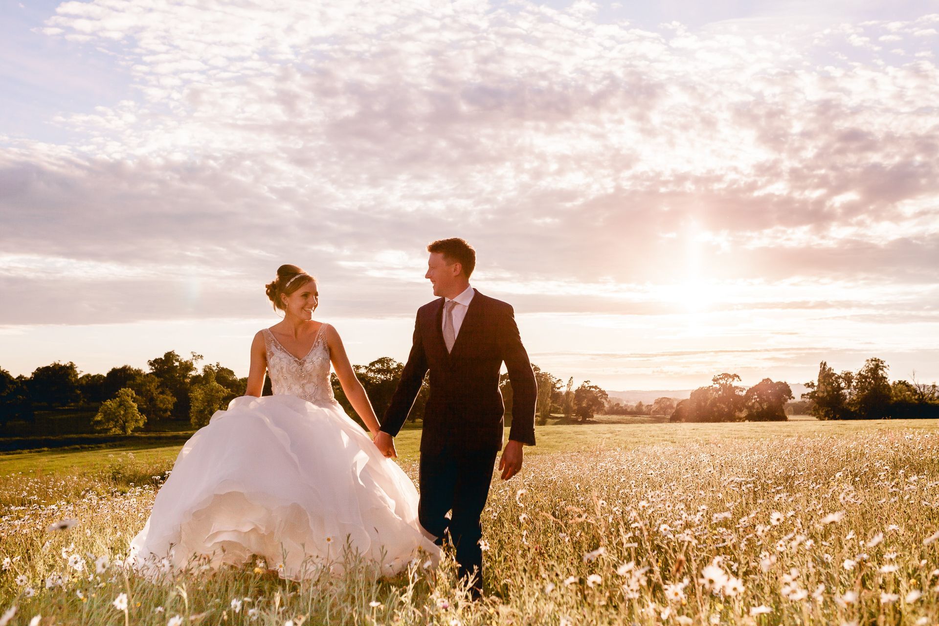 a bride and groom are walking through a field of flowers holding hands .
