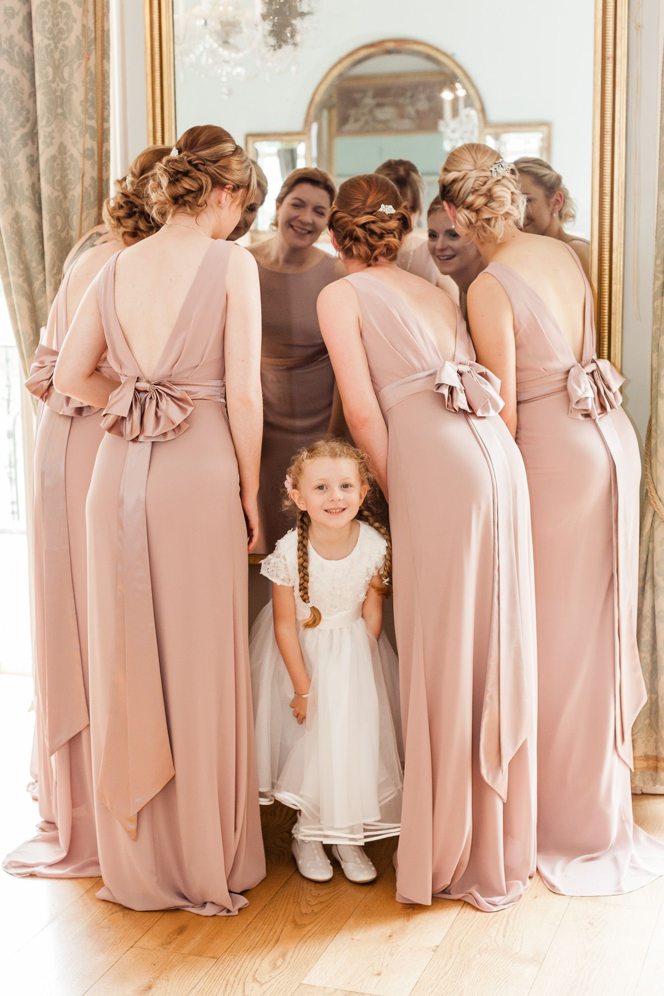 a group of bridesmaids and a flower girl are standing in front of a mirror.