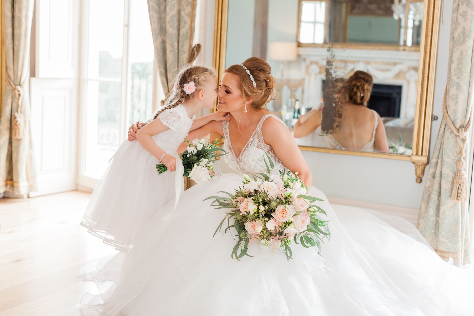 a bride and her flower girl are kissing in front of a mirror.