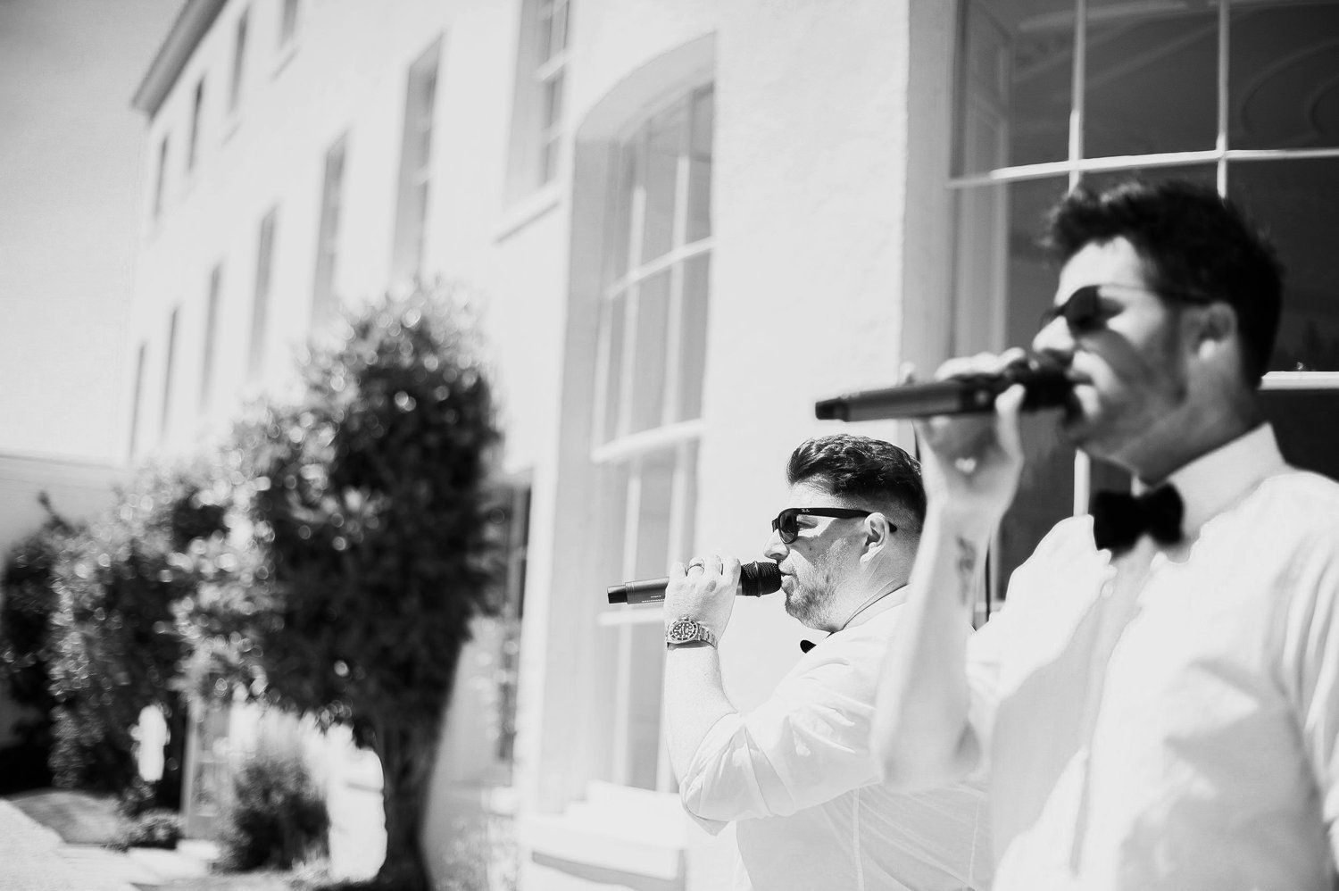 two men are singing into microphones in front of a building .
