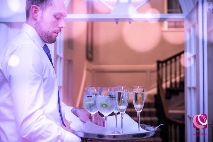 a man in a white shirt and tie is holding a tray of wine glasses .