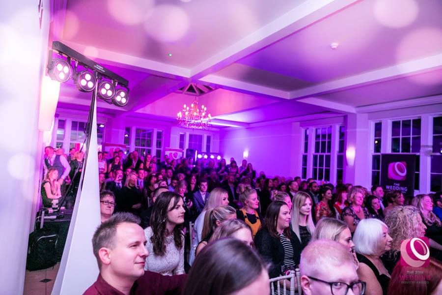 a large group of people are standing in a room with purple lights .