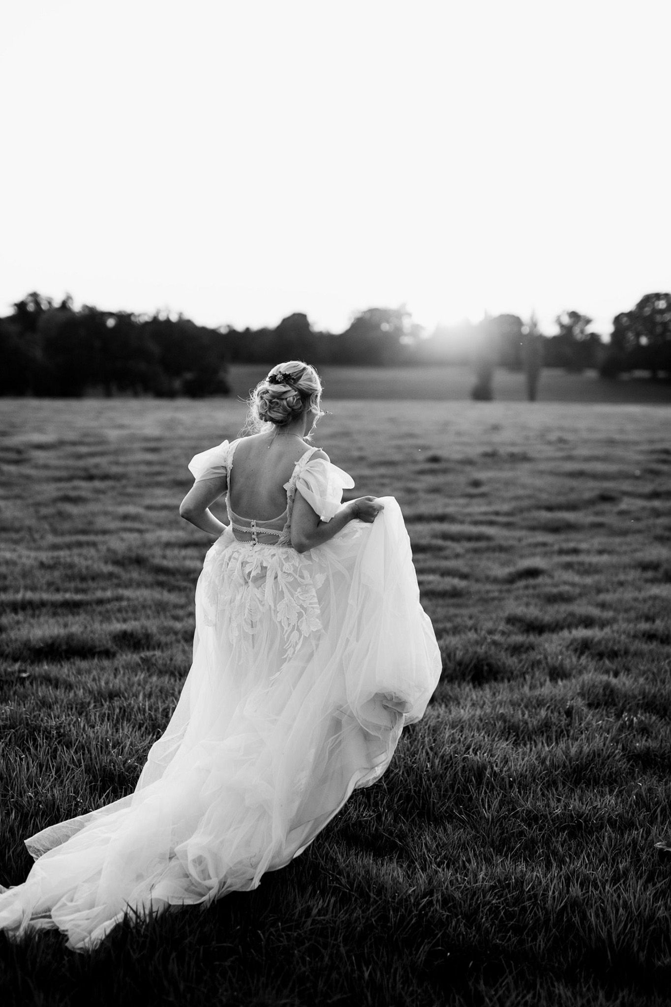 a black and white photo of a bride in a wedding dress running through a field .