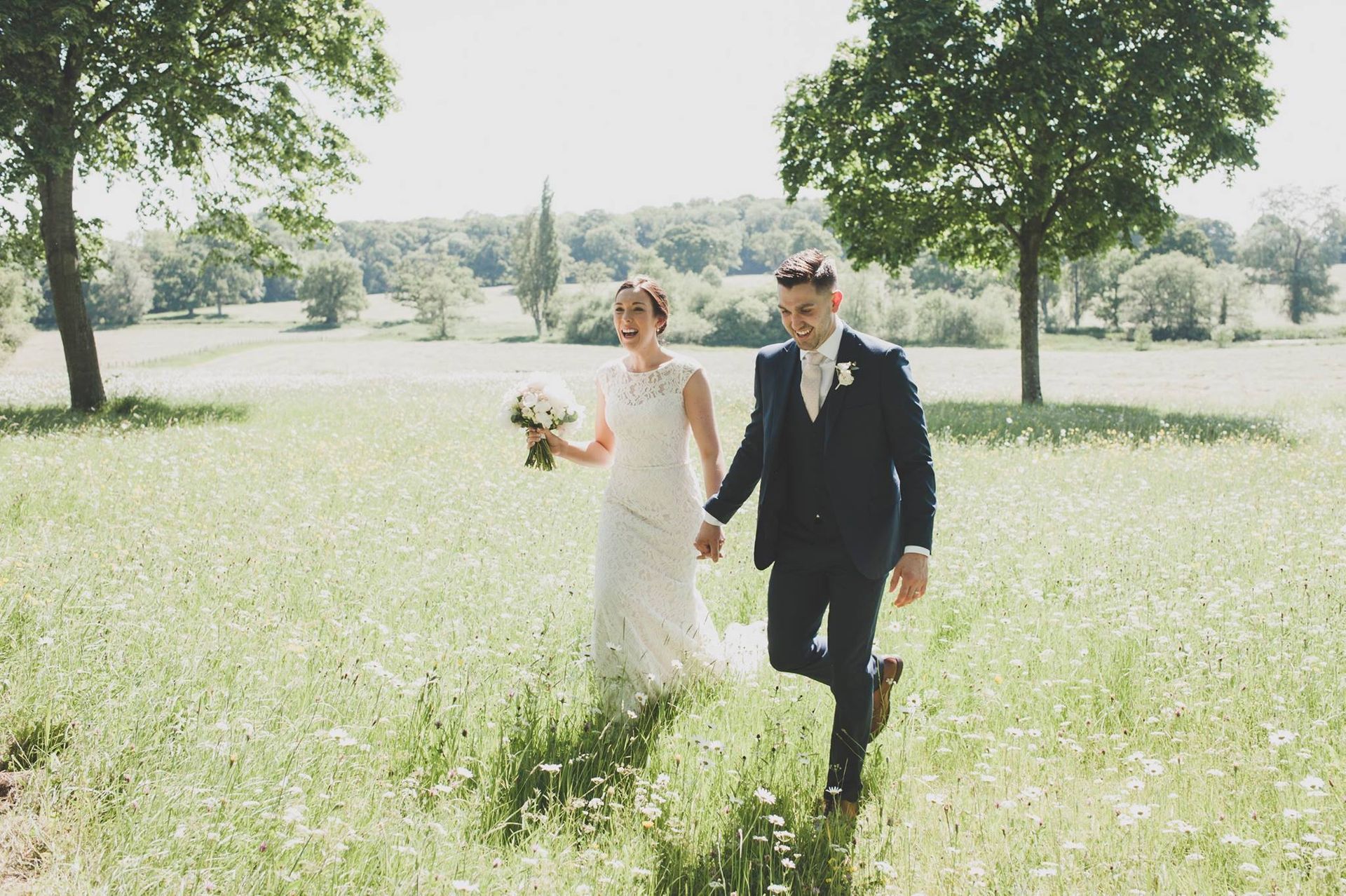 a bride and groom are walking through a field holding hands .