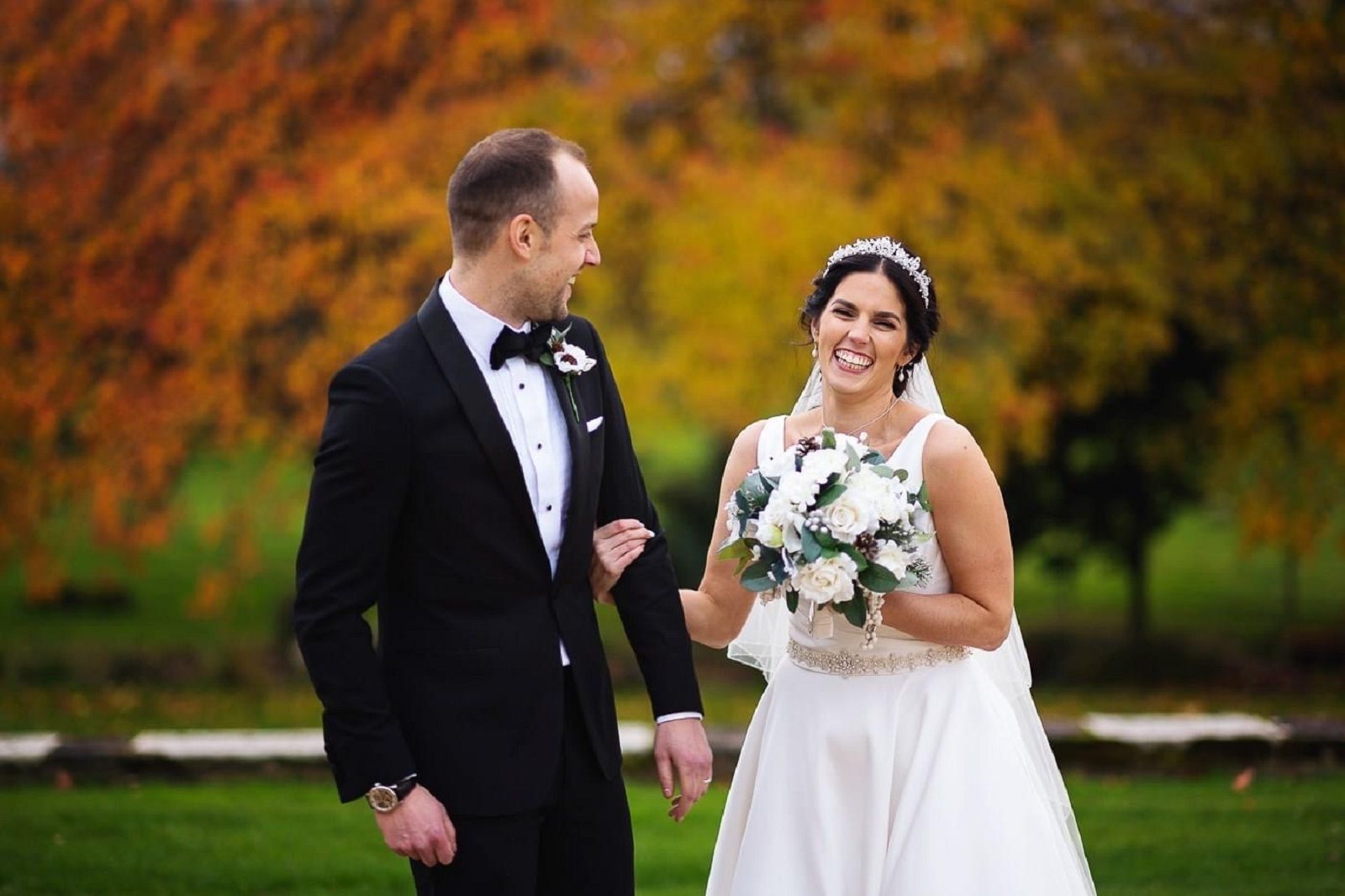 a bride and groom are standing next to each other in a park holding hands .