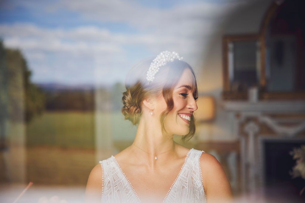 the bride is wearing a tiara and smiling while looking out the window .