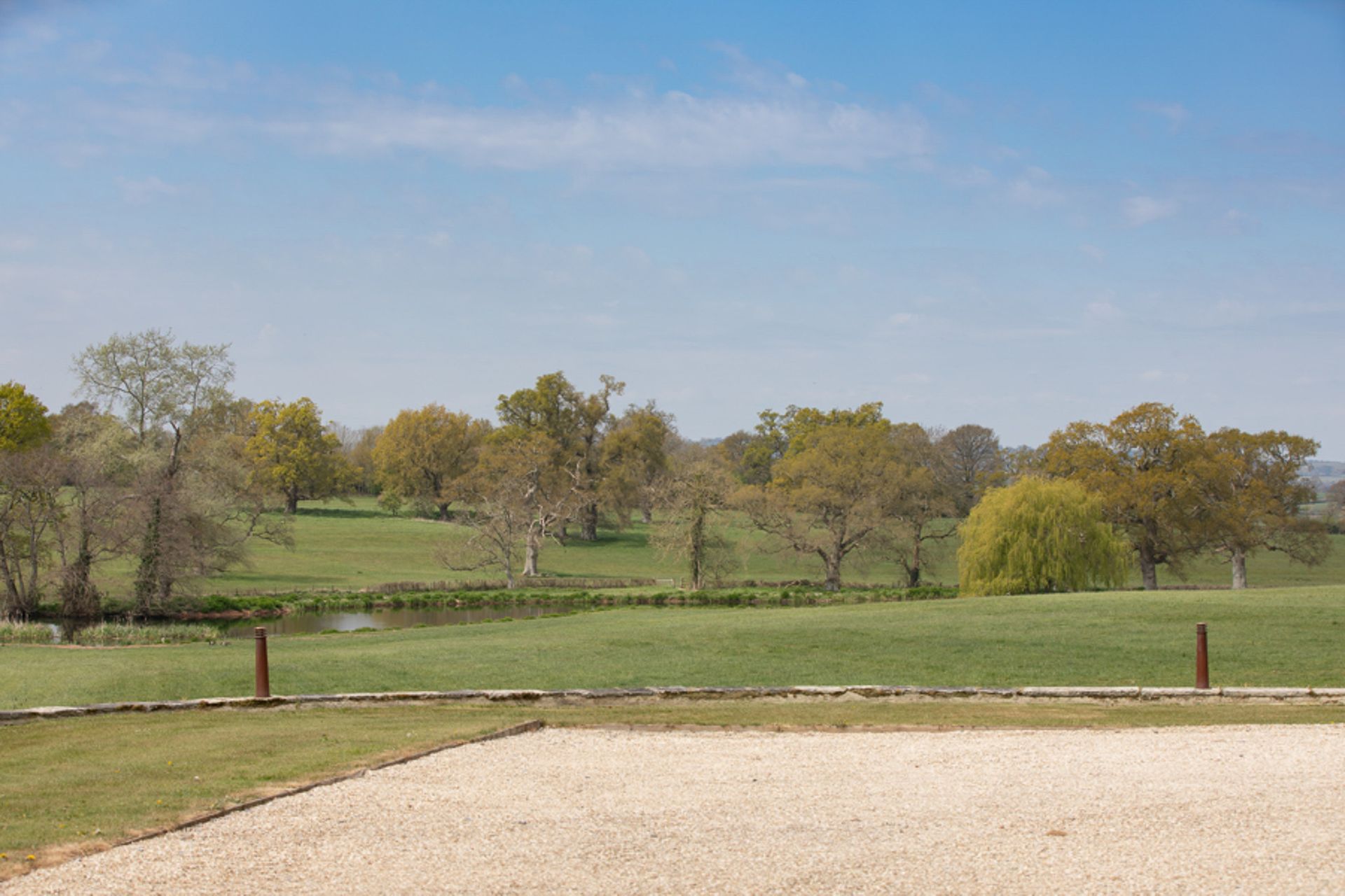 a gravel driveway leading to a grassy field with trees in the background .