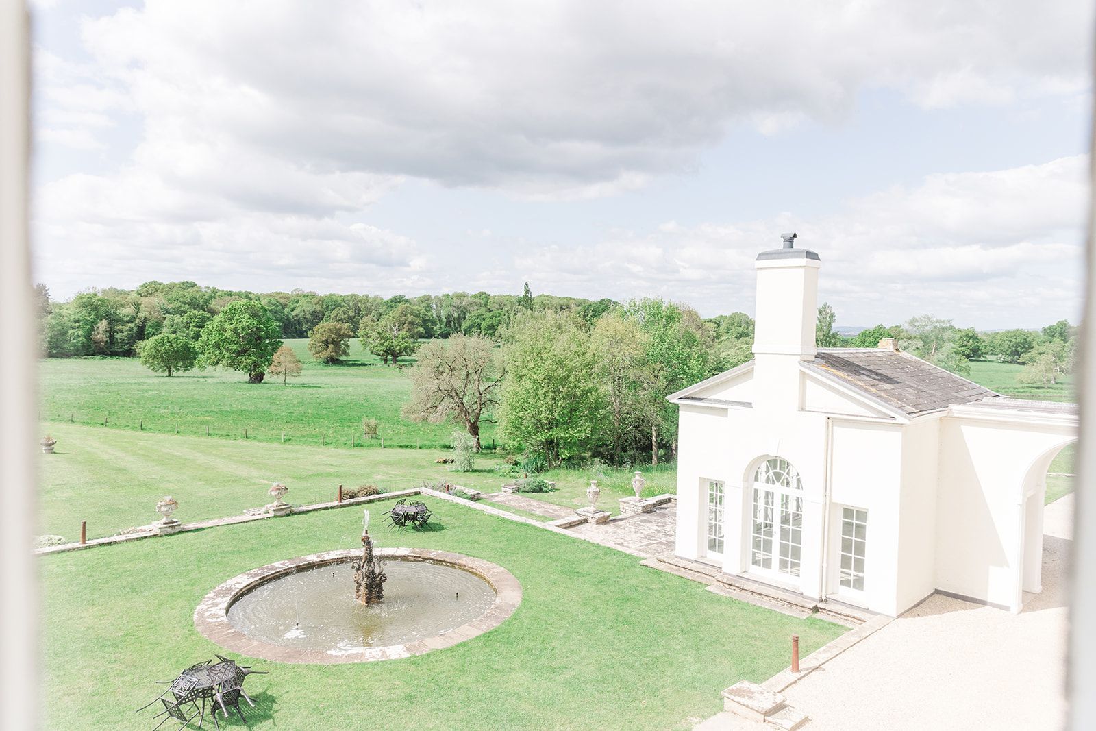 an aerial view of a white house with a fountain in the middle of a lush green field .