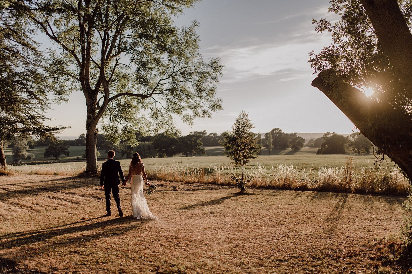 a bride and groom are walking in a field holding hands .