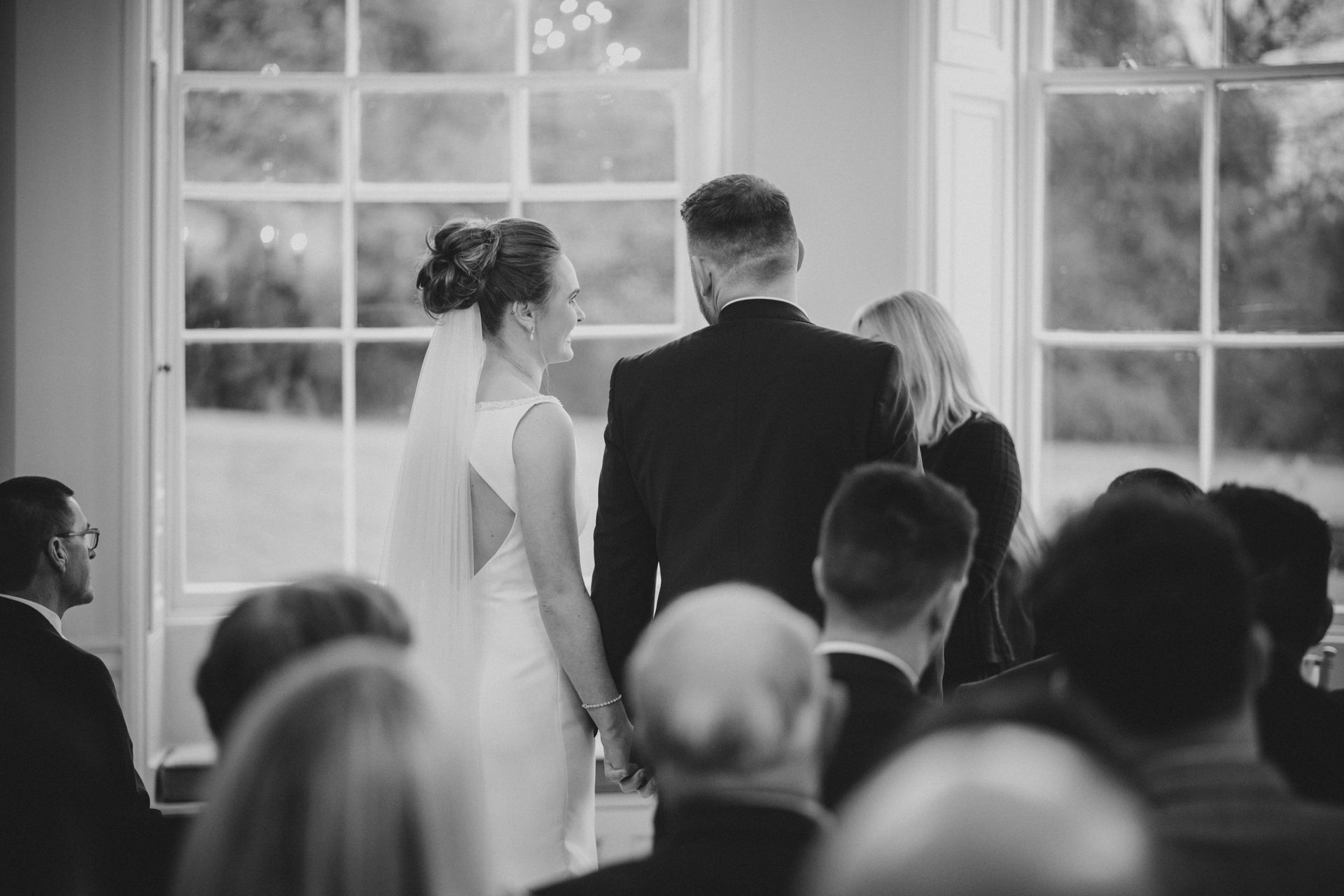 a black and white photo of a bride and groom holding hands during their wedding ceremony .