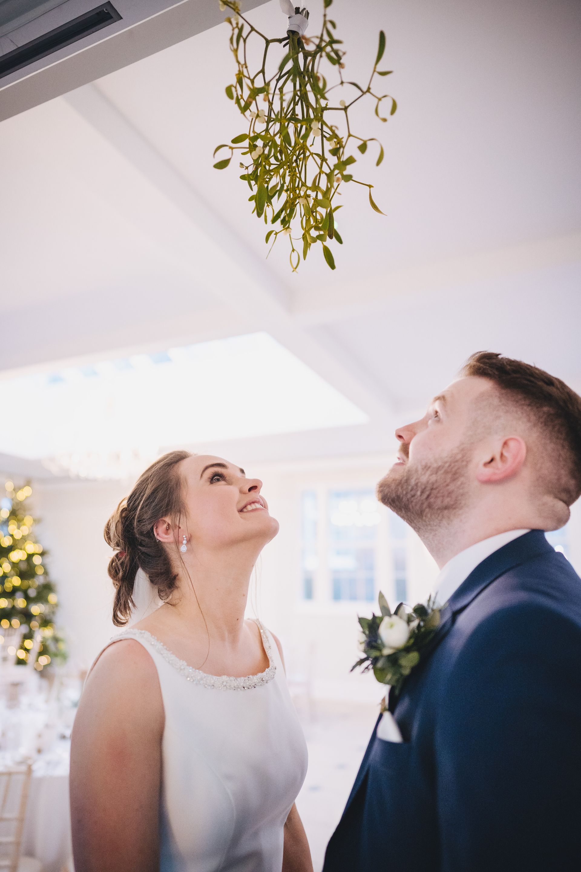 a bride and groom are looking up at mistletoe hanging from the ceiling .