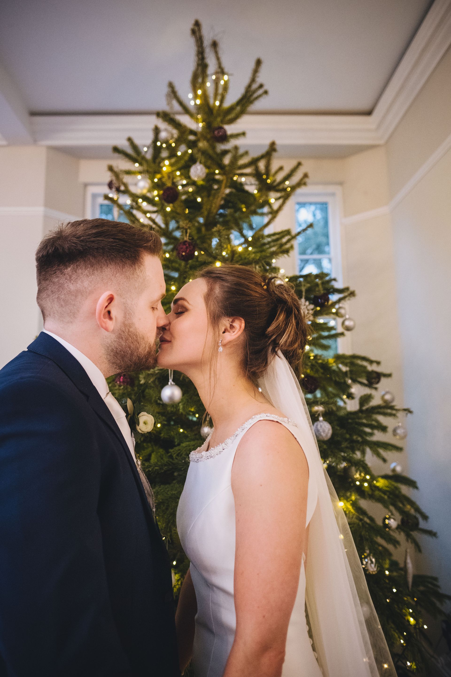 a bride and groom kissing in front of a christmas tree .