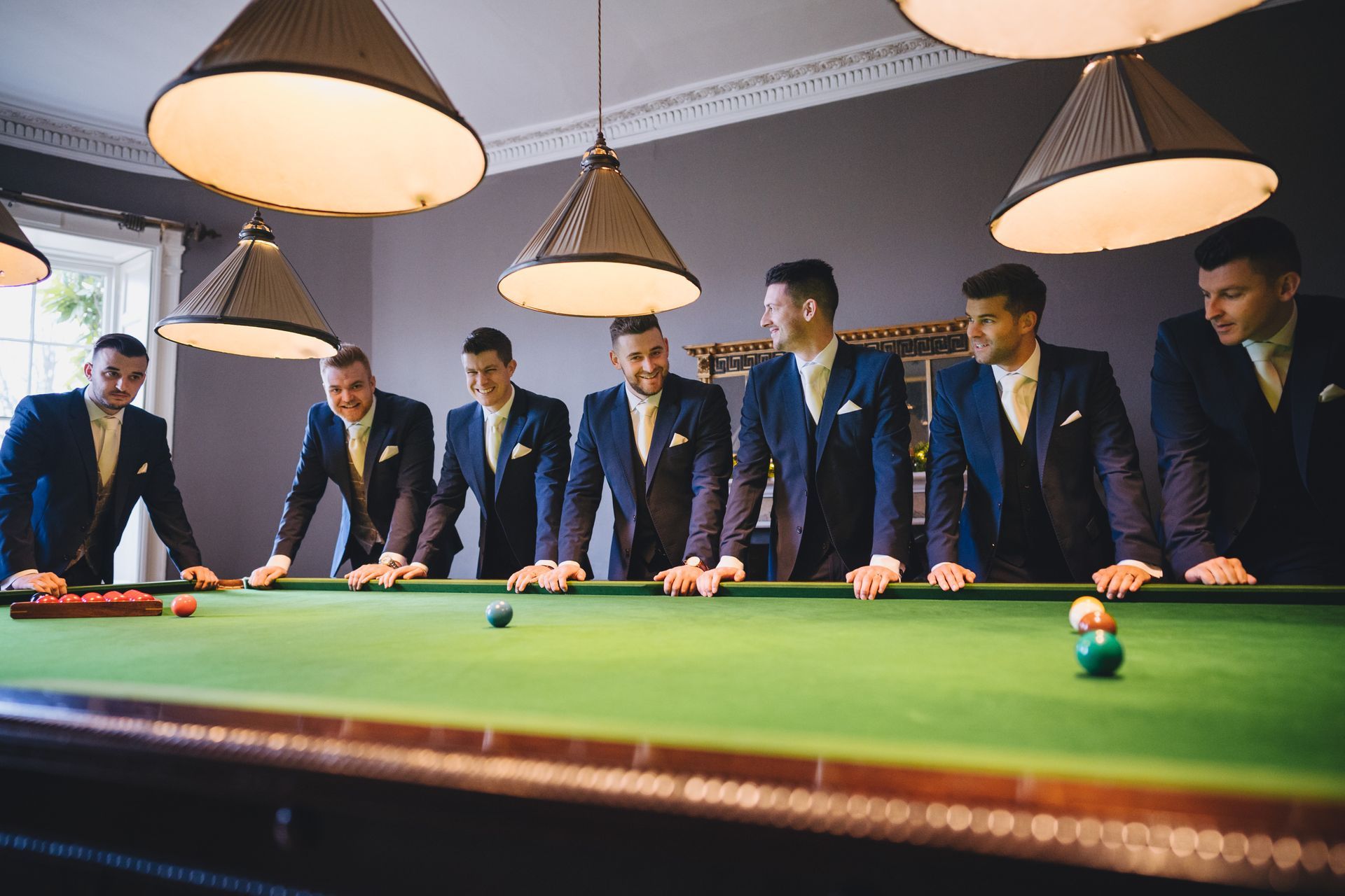 a group of men in suits are standing around a pool table .