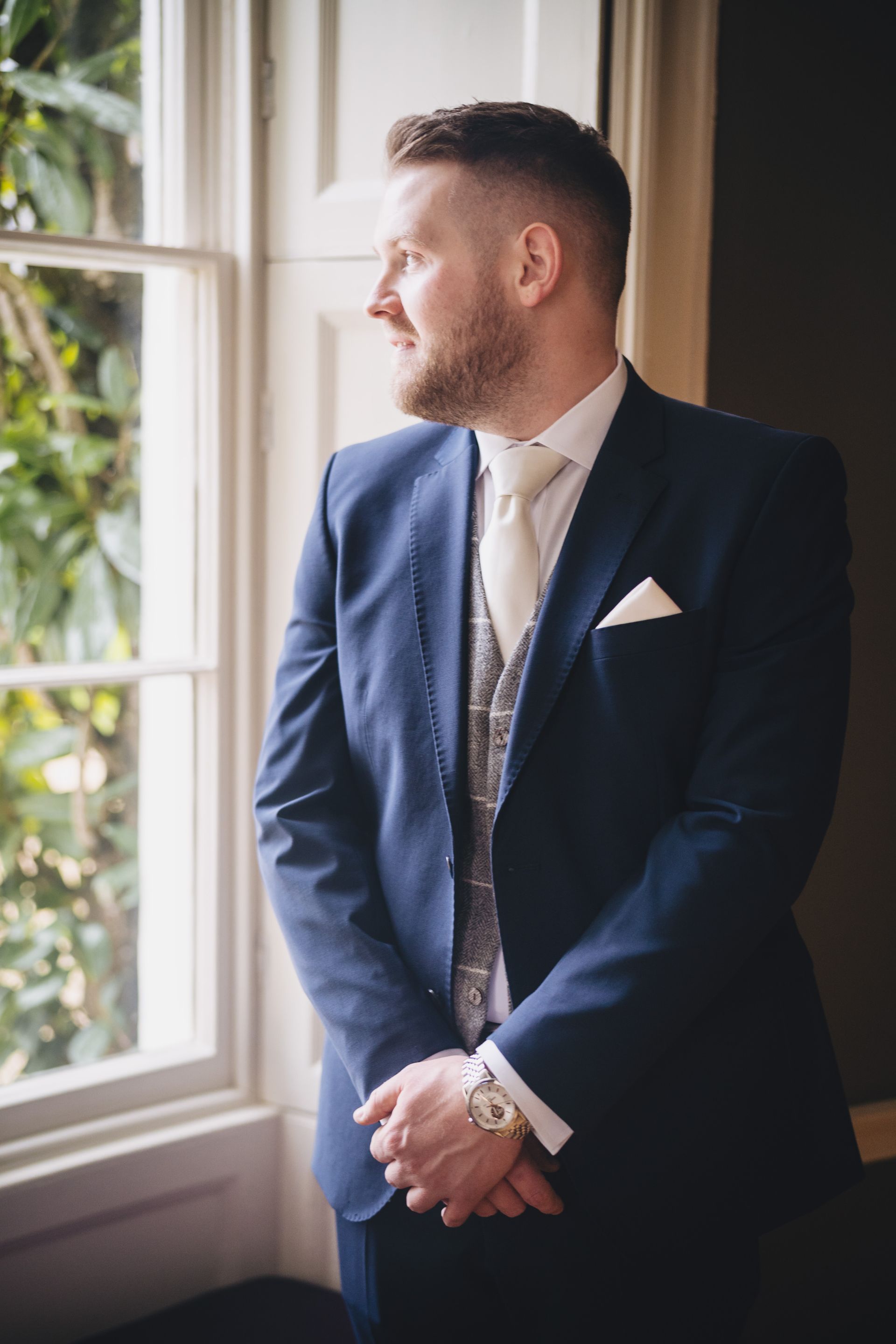 a man in a suit and tie is standing in front of a window.