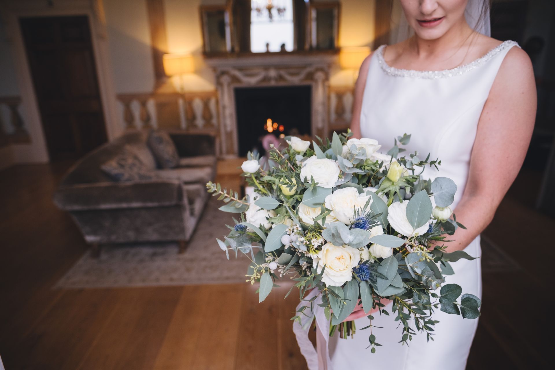 a bride in a white dress is holding a bouquet of flowers in front of a fireplace .